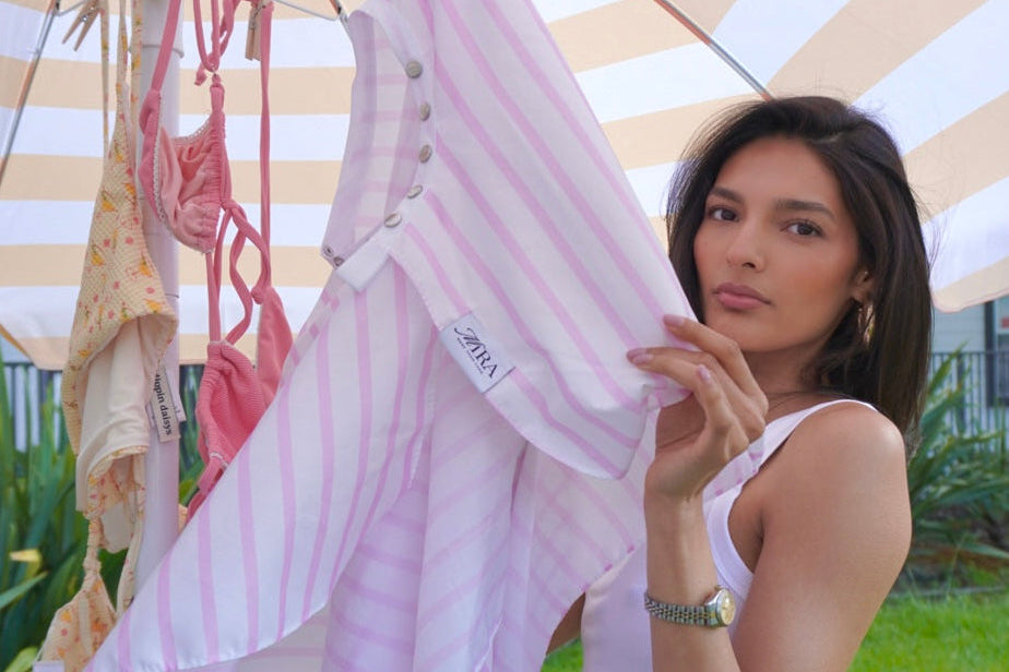 Woman holding a white garment with a striped umbrella in the background