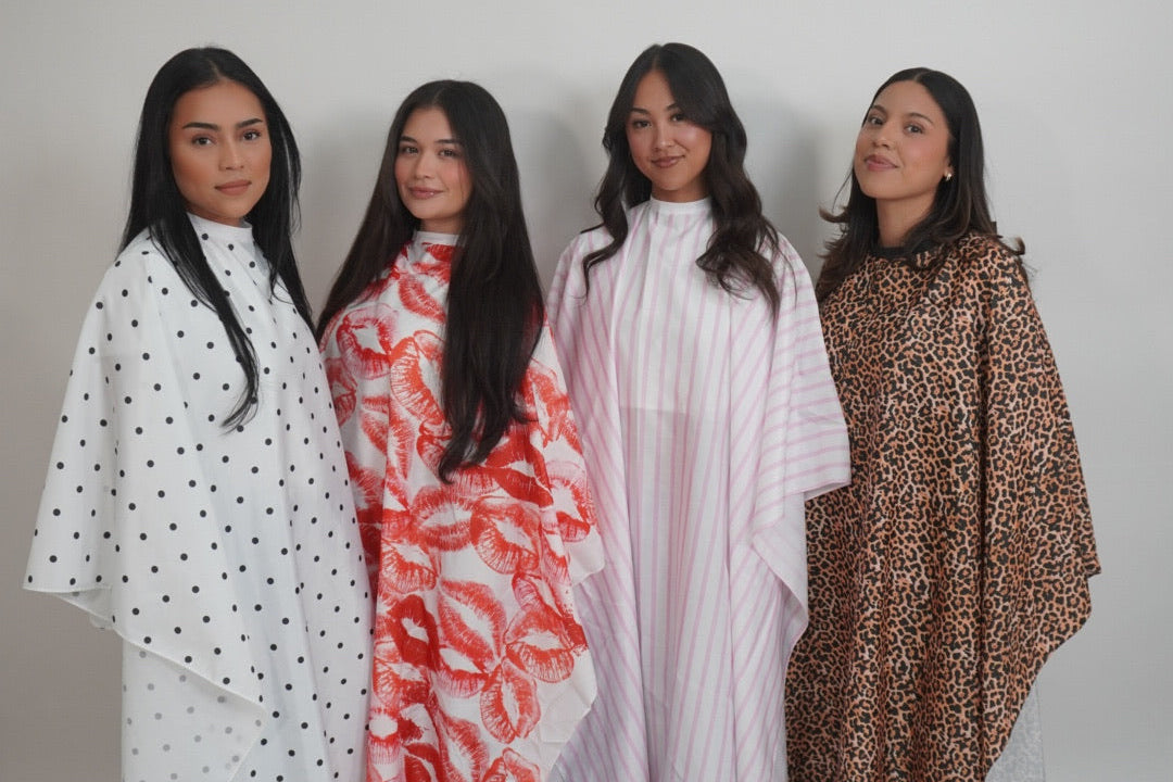 Four women standing side by side wearing different poncho-style outerwear garments: white with black polka dots, red and orange abstract print, pale pink vertical stripes, and brown leopard print, against a plain light gray studio background.